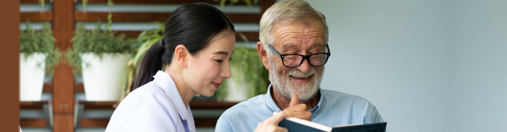 A caregiver and an elderly man reading a book