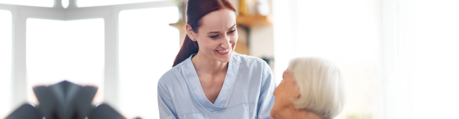 A female caregiver smiling to an elderly woman