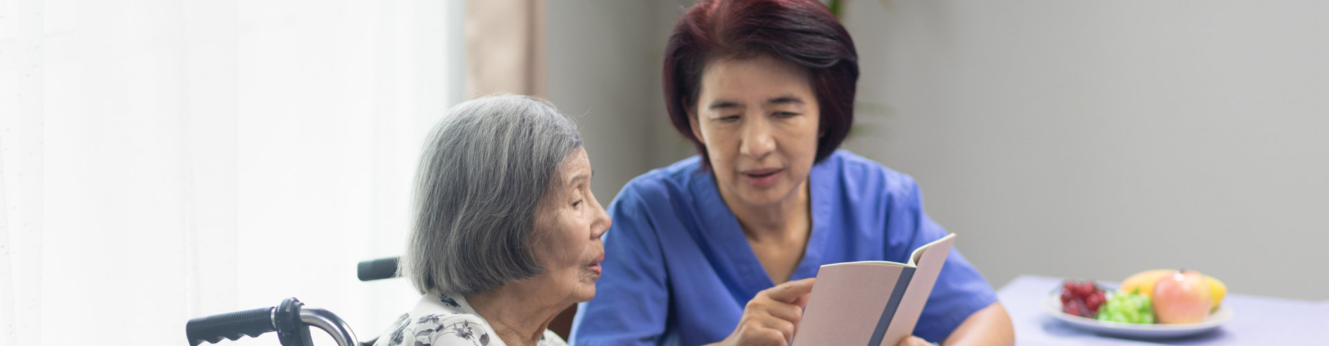 Female caregiver helping an elderly woman to read